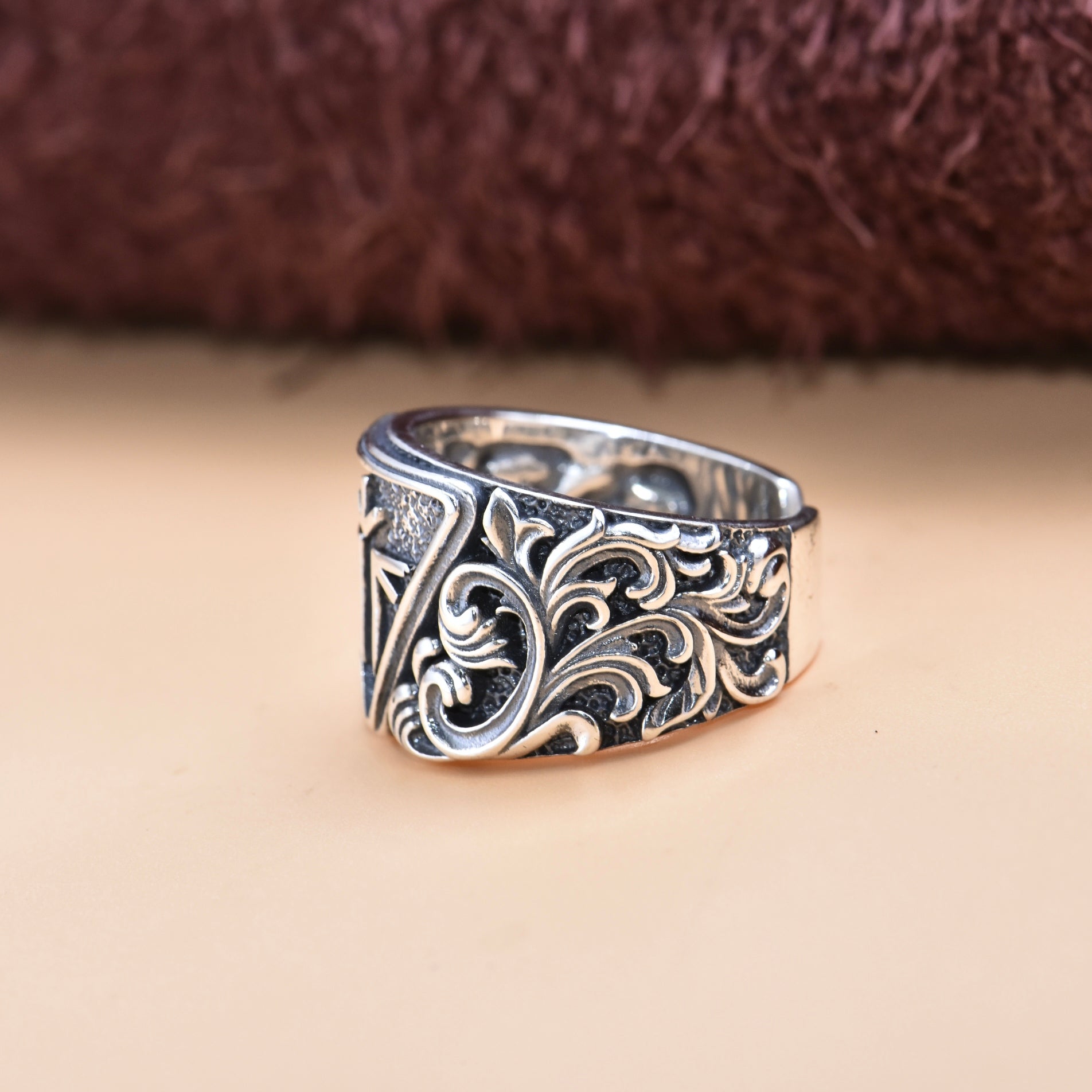 Intricately designed silver ring with a geometric emblem and ornamental accents.